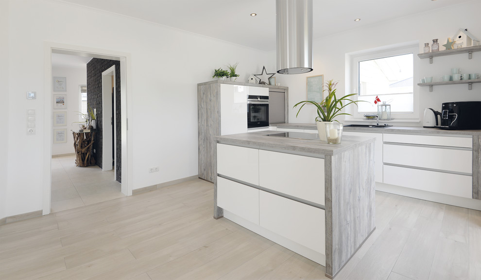 This is an example of a scandi l-shaped open plan kitchen in Berlin with a built-in sink, recessed-panel cabinets, white cabinets, wood worktops, white splashback, stainless steel appliances, light hardwood flooring and an island.