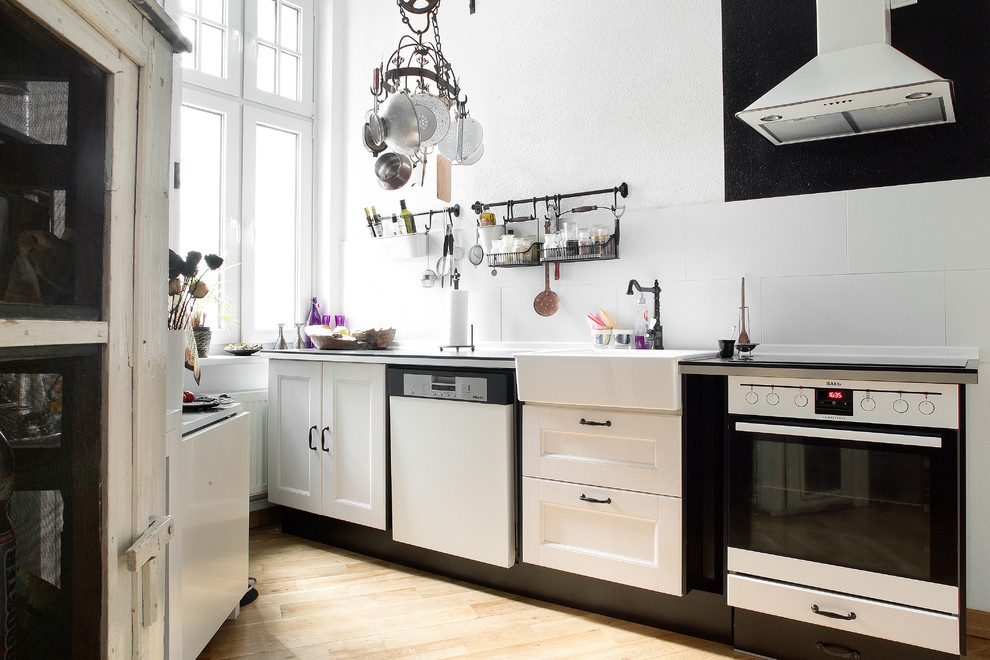 Geschlossene, Einzeilige Stilmix Küche ohne Insel mit Einbauwaschbecken, weißen Schränken, Rückwand aus Keramikfliesen, weißen Elektrogeräten und hellem Holzboden in Berlin