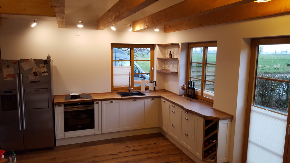 Inspiration for a medium sized rural l-shaped enclosed kitchen in Hamburg with a built-in sink, raised-panel cabinets, white cabinets, wood worktops, white splashback, black appliances, light hardwood flooring, no island and brown floors.