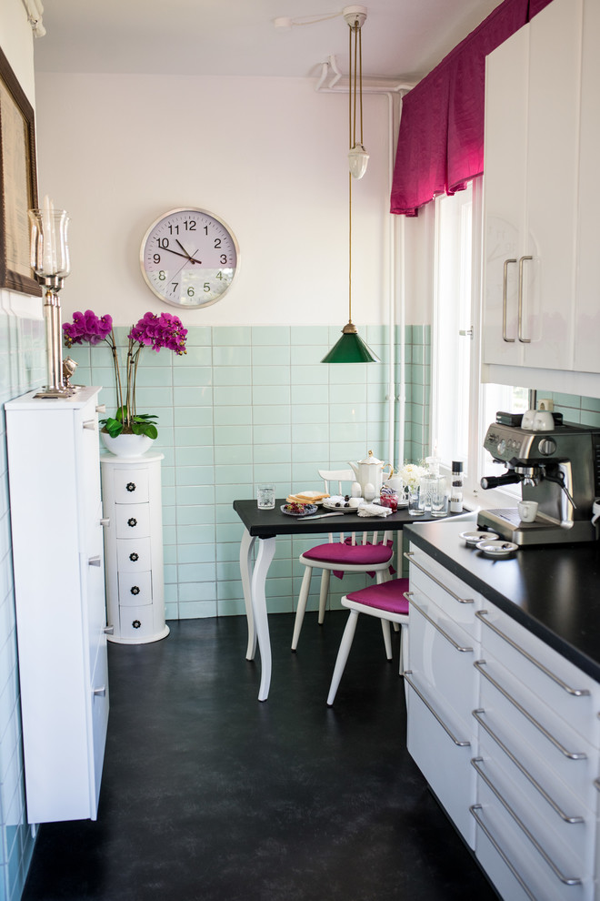 Mid-sized 1960s galley black floor and linoleum floor enclosed kitchen photo in Berlin with white cabinets, black countertops, flat-panel cabinets, green backsplash, ceramic backsplash and no island