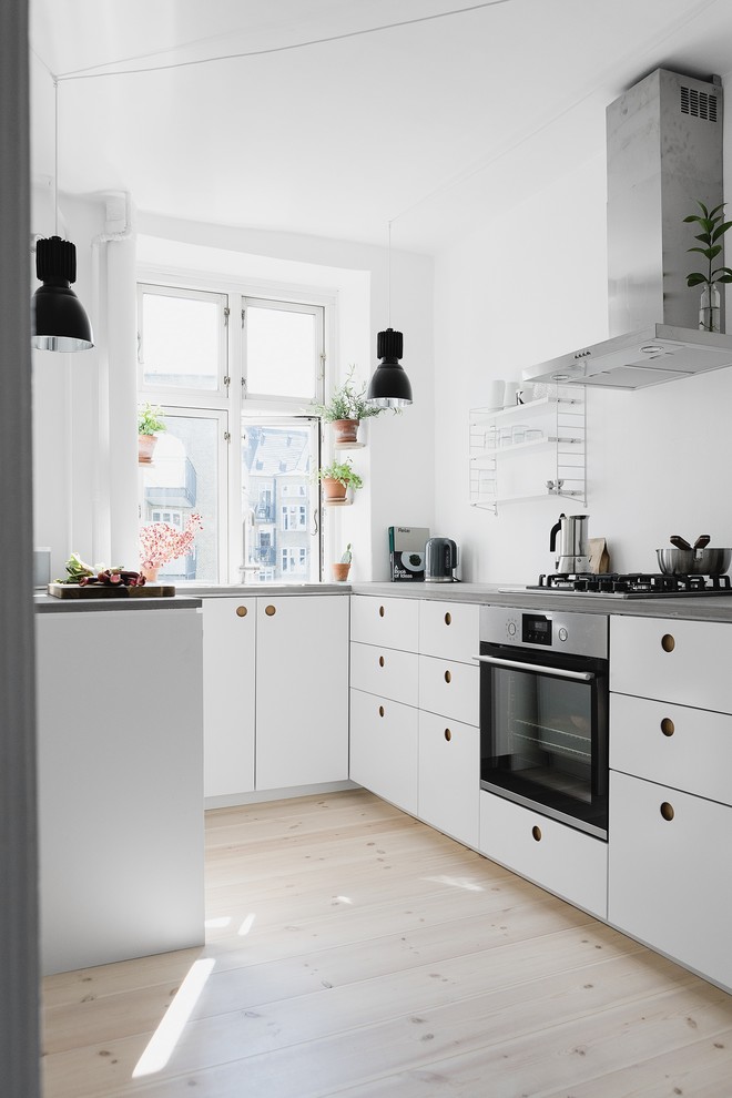 Small scandinavian u-shaped open plan kitchen in Berlin with flat-panel cabinets, white cabinets, concrete worktops, white splashback, light hardwood flooring, no island and stainless steel appliances.