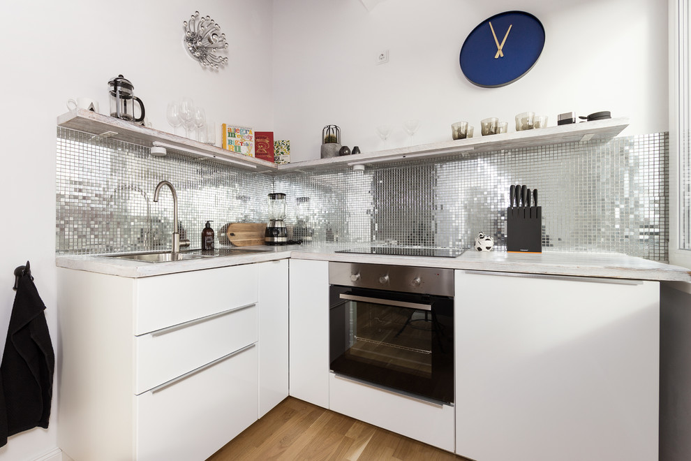 Inspiration for a small contemporary l-shaped open plan kitchen in Berlin with a built-in sink, flat-panel cabinets, white cabinets, wood worktops, metallic splashback, mosaic tiled splashback, stainless steel appliances, medium hardwood flooring and no island.
