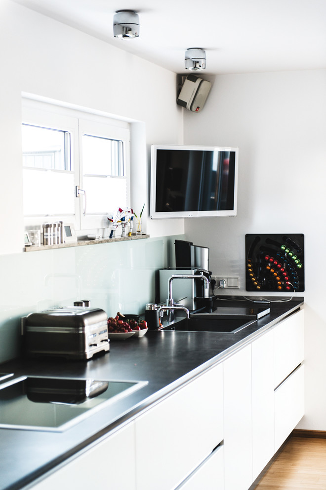 ニュルンベルクにある高級な巨大なコンテンポラリースタイルのおしゃれなキッチン (ダブルシンク、フラットパネル扉のキャビネット、白いキャビネット、人工大理石カウンター、白いキッチンパネル、ガラス板のキッチンパネル、シルバーの調理設備、竹フローリング、アイランドなし) の写真