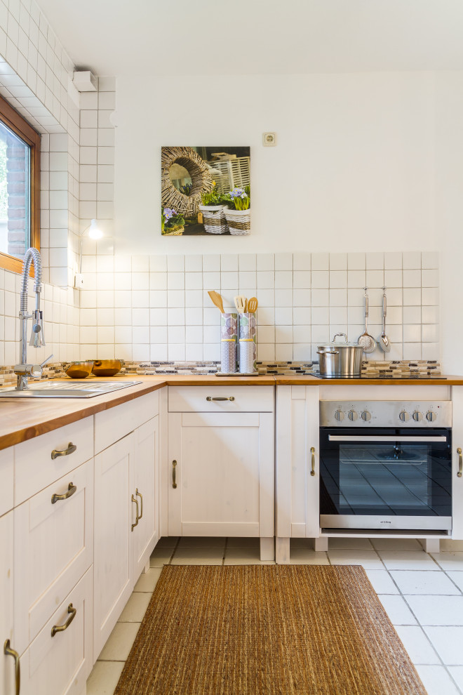 Design ideas for a classic l-shaped kitchen in Other with a built-in sink, shaker cabinets, white cabinets, wood worktops, white splashback, stainless steel appliances, white floors and brown worktops.