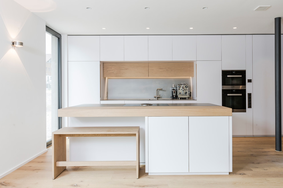 Expansive contemporary galley open plan kitchen in Munich with an integrated sink, flat-panel cabinets, white cabinets, stainless steel worktops, medium hardwood flooring and an island.