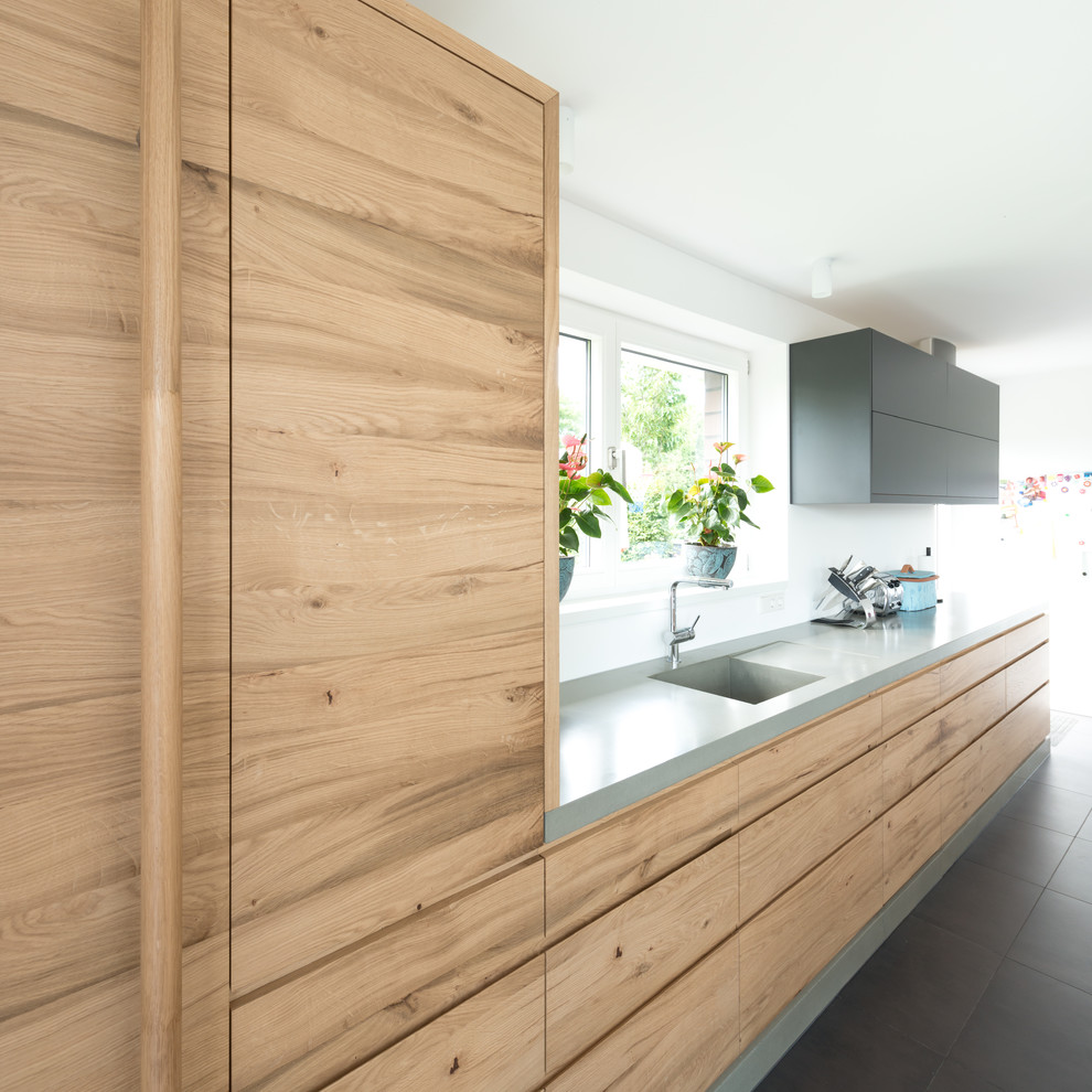 Inspiration for a medium sized contemporary single-wall open plan kitchen in Other with a single-bowl sink, flat-panel cabinets, light wood cabinets, concrete worktops, white splashback, an island, grey floors, black appliances and ceramic flooring.