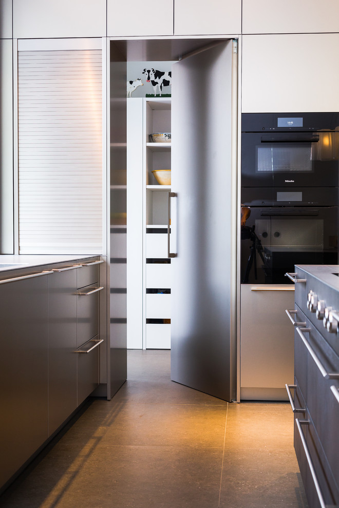 Inredning av ett modernt stort grå linjärt grått kök med öppen planlösning, med släta luckor, skåp i rostfritt stål, bänkskiva i rostfritt stål, en integrerad diskho, stänkskydd med metallisk yta, rostfria vitvaror och en köksö