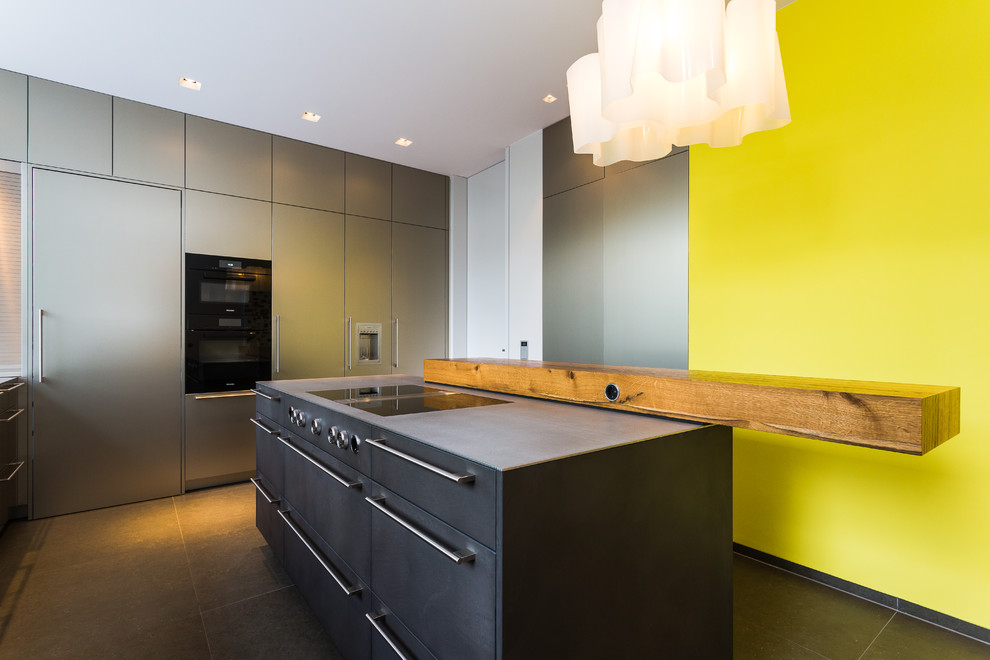 フランクフルトにあるラグジュアリーな広いコンテンポラリースタイルのおしゃれなキッチン (一体型シンク、フラットパネル扉のキャビネット、ヴィンテージ仕上げキャビネット、ステンレスカウンター、黄色いキッチンパネル、シルバーの調理設備、グレーの床、グレーのキッチンカウンター) の写真