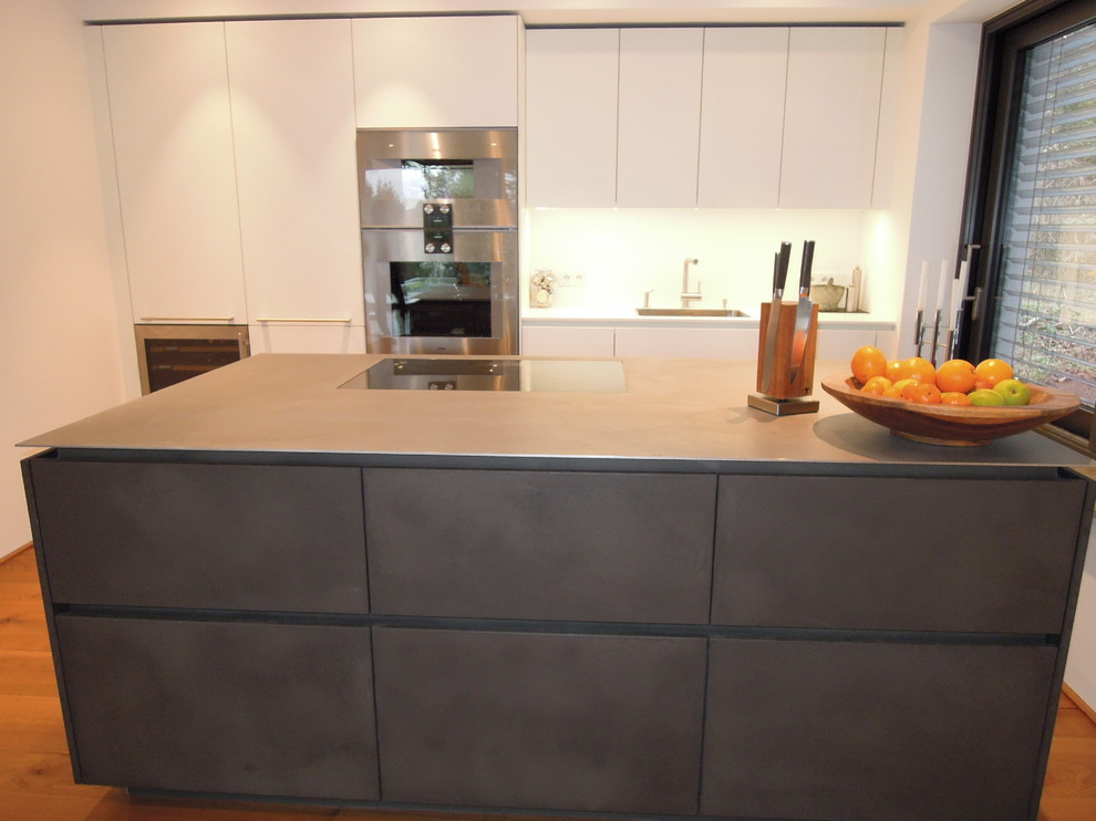 Inspiration for a medium sized contemporary kitchen in Frankfurt with black cabinets, concrete worktops, stainless steel appliances, light hardwood flooring and an island.