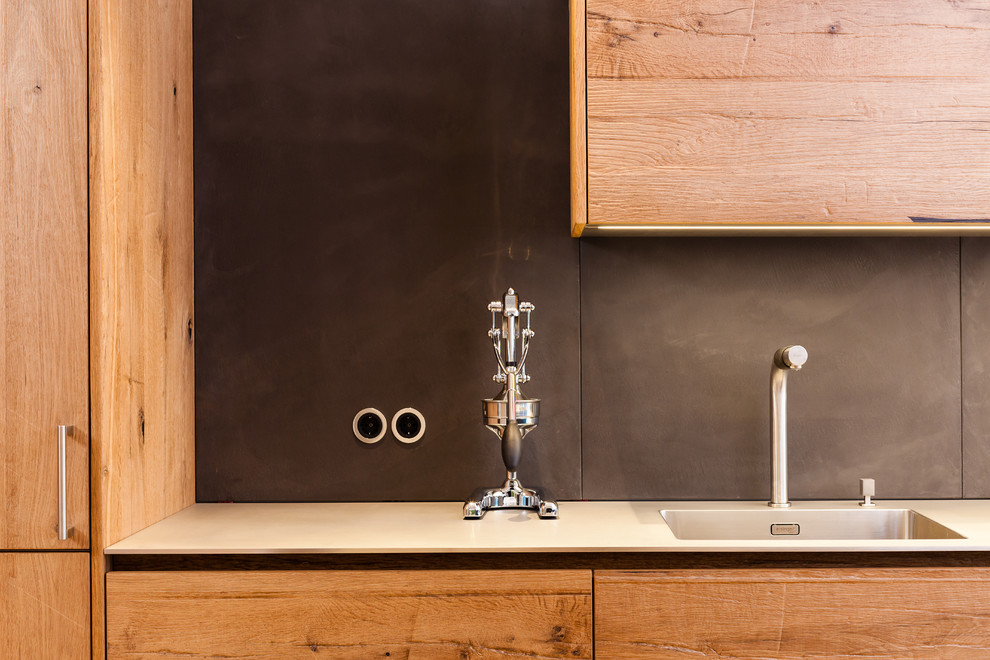 フランクフルトにあるコンテンポラリースタイルのおしゃれなキッチン (中間色木目調キャビネット、黒いキッチンパネル、シルバーの調理設備) の写真