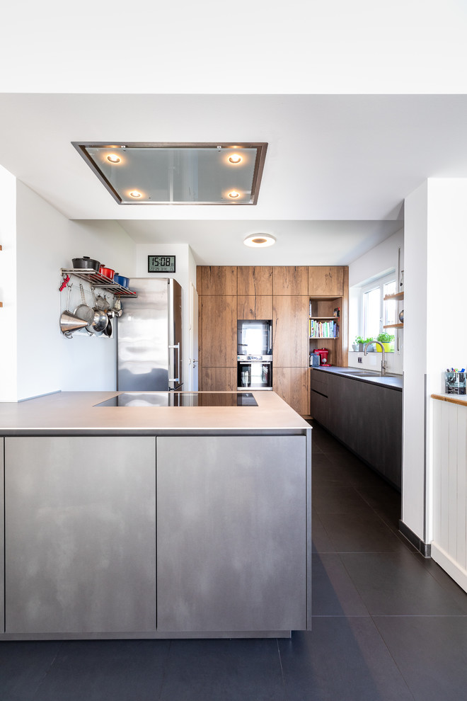 Idéer för ett stort modernt grå kök, med en integrerad diskho, släta luckor, skåp i rostfritt stål, bänkskiva i rostfritt stål, vitt stänkskydd, glaspanel som stänkskydd, svarta vitvaror, en köksö och svart golv