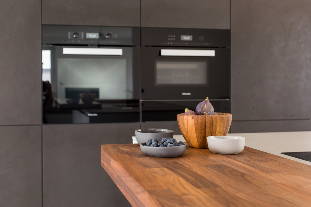 Esempio di una grande cucina minimal con lavello integrato, ante lisce, ante bianche, top in superficie solida, paraspruzzi a finestra, elettrodomestici neri, pavimento grigio e top grigio