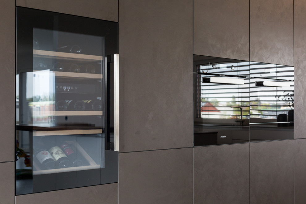 Modelo de cocinas en L contemporánea grande abierta con fregadero integrado, armarios con paneles lisos, puertas de armario blancas, encimera de acrílico, salpicadero de vidrio, electrodomésticos negros, una isla, suelo gris y encimeras grises