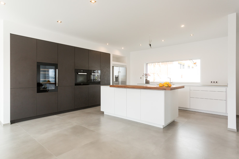 Large contemporary l-shaped open plan kitchen in Frankfurt with an integrated sink, flat-panel cabinets, white cabinets, composite countertops, black appliances, an island, grey floors, grey worktops and white splashback.