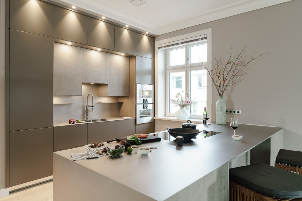 Große Moderne Wohnküche mit flächenbündigen Schrankfronten, Küchengeräten aus Edelstahl, grauer Arbeitsplatte, braunem Holzboden, Halbinsel und Edelstahl-Arbeitsplatte in Hamburg