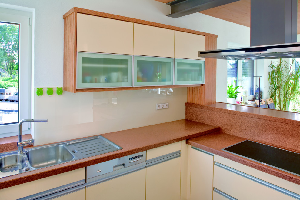 Bild på ett mellanstort funkis brun brunt kök, med en nedsänkt diskho, beige skåp, bänkskiva i koppar, vitt stänkskydd, glaspanel som stänkskydd, rostfria vitvaror, mörkt trägolv och brunt golv