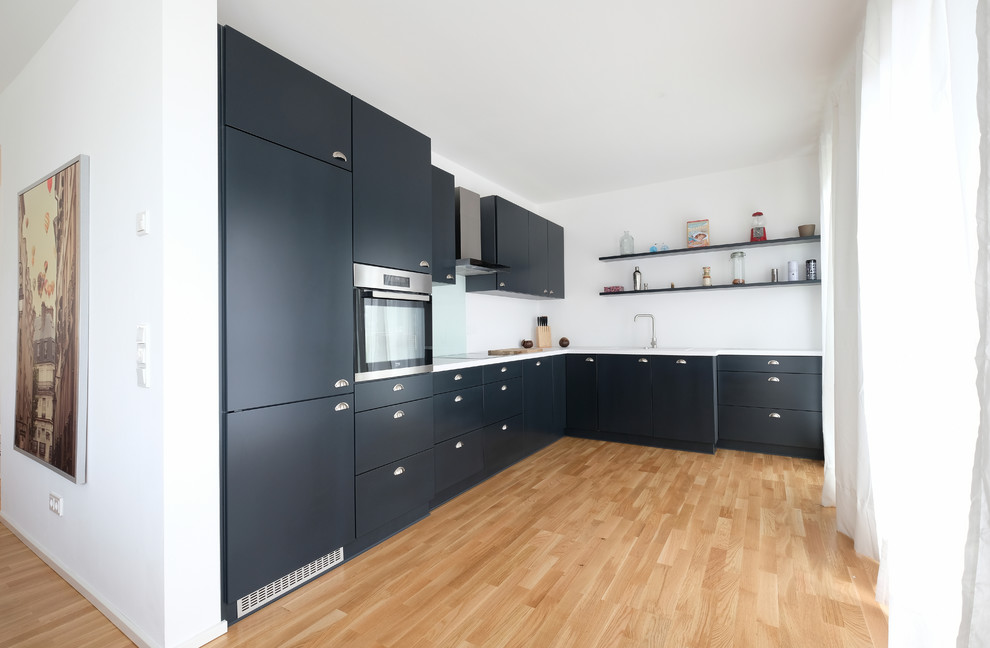 Inspiration for a medium sized contemporary l-shaped open plan kitchen in Cologne with a built-in sink, flat-panel cabinets, blue cabinets, blue splashback, glass sheet splashback, stainless steel appliances, medium hardwood flooring, no island and brown floors.