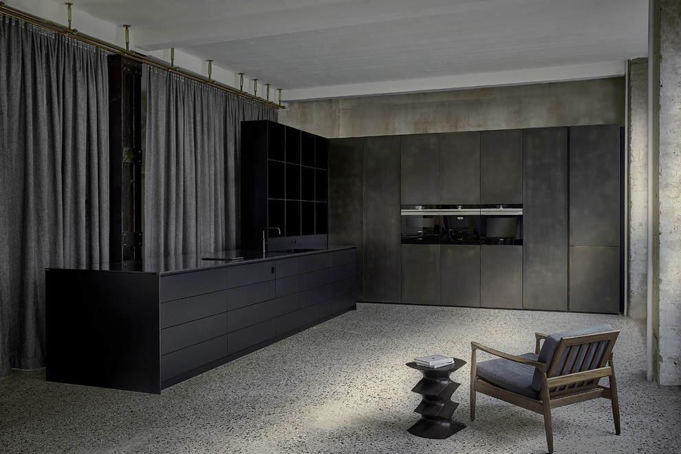 Foto på ett avskilt, stort industriellt svart l-kök, med en integrerad diskho, släta luckor, svarta skåp, svarta vitvaror, en halv köksö och grått golv