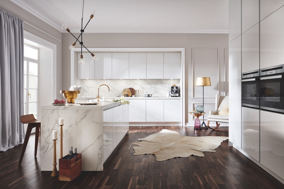 Inspiration för ett stort funkis vit vitt kök, med en integrerad diskho, släta luckor, vita skåp, marmorbänkskiva, vitt stänkskydd, stänkskydd i marmor, svarta vitvaror, mörkt trägolv, en köksö och brunt golv