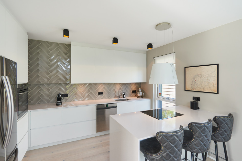 Photo of a medium sized scandi l-shaped kitchen/diner in Berlin with a single-bowl sink, flat-panel cabinets, white cabinets, beige splashback, ceramic splashback, stainless steel appliances, light hardwood flooring, an island and white worktops.
