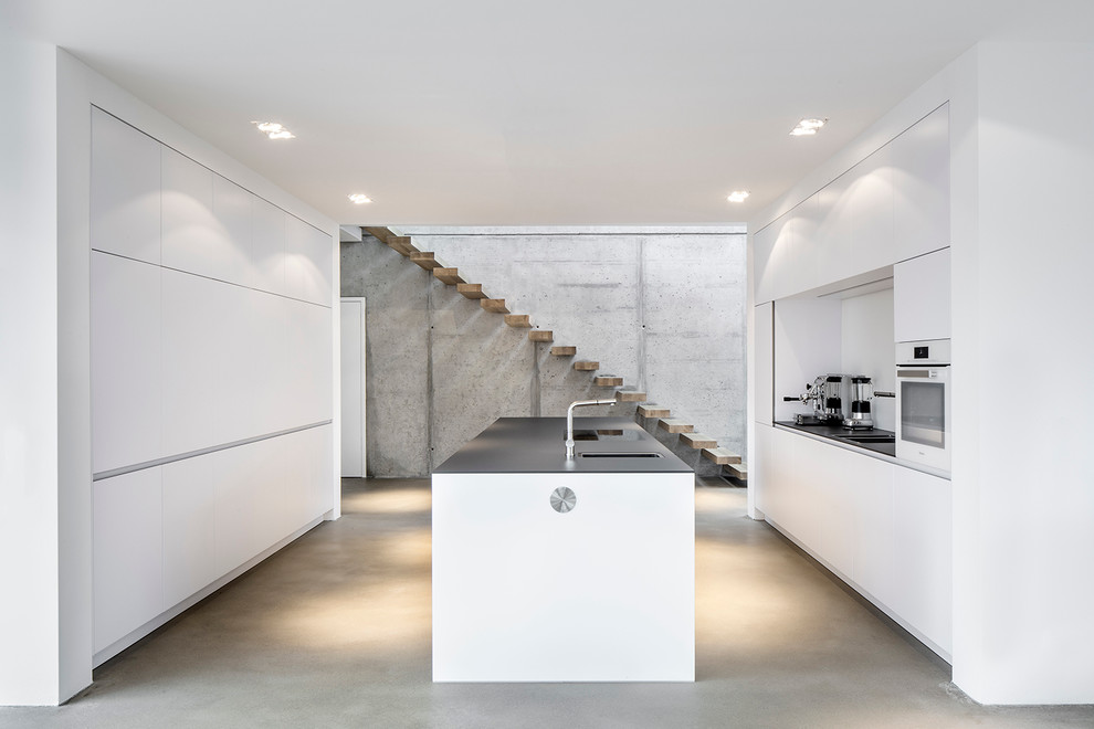 Immagine di una cucina minimalista di medie dimensioni con ante lisce, paraspruzzi bianco, lavello a vasca singola e pavimento in cemento