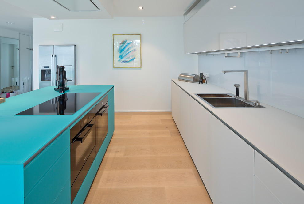 Inspiration for a mid-sized contemporary galley light wood floor and brown floor open concept kitchen remodel in Dusseldorf with a drop-in sink, flat-panel cabinets, blue cabinets, glass countertops, blue backsplash, glass sheet backsplash, black appliances and two islands