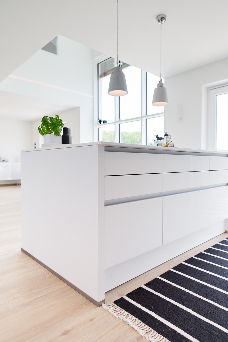 Idéer för att renovera ett stort minimalistiskt kök med öppen planlösning, med en undermonterad diskho, släta luckor, vita skåp, bänkskiva i kvartsit, svart stänkskydd, glaspanel som stänkskydd, svarta vitvaror, vinylgolv, en köksö och beiget golv