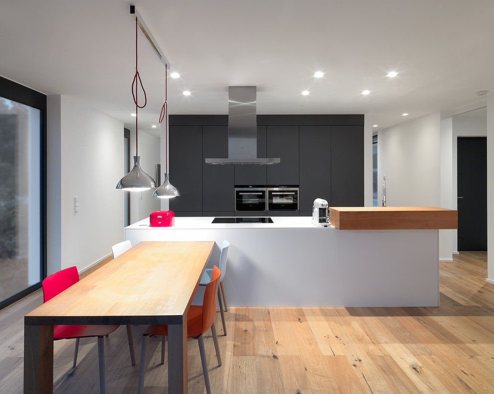 Offene, Große Moderne Küche in grau-weiß mit hellem Holzboden, flächenbündigen Schrankfronten, schwarzen Schränken, Küchengeräten aus Edelstahl und Kücheninsel in Berlin