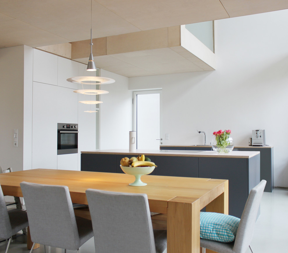 Стильный дизайн: кухня-гостиная среднего размера в скандинавском стиле с островом, плоскими фасадами, белыми фасадами, техникой из нержавеющей стали, одинарной мойкой и белым фартуком - последний тренд