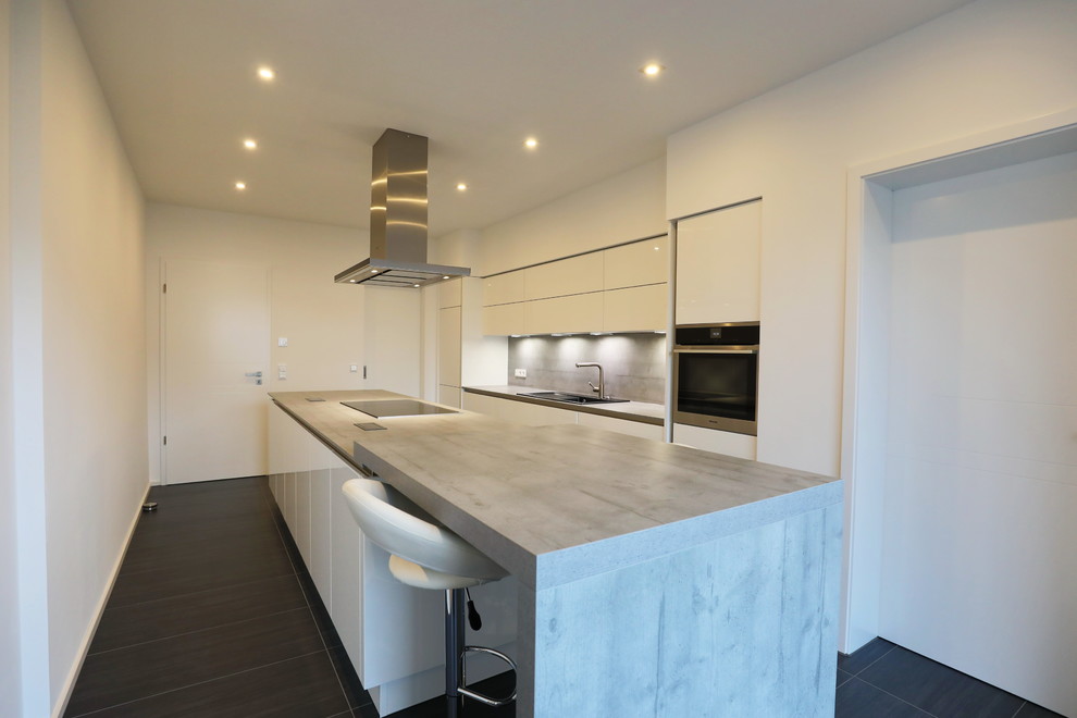 Photo of a medium sized scandi galley enclosed kitchen in Other with a built-in sink, flat-panel cabinets, white cabinets, concrete worktops, grey splashback, black appliances, an island, black floors and grey worktops.