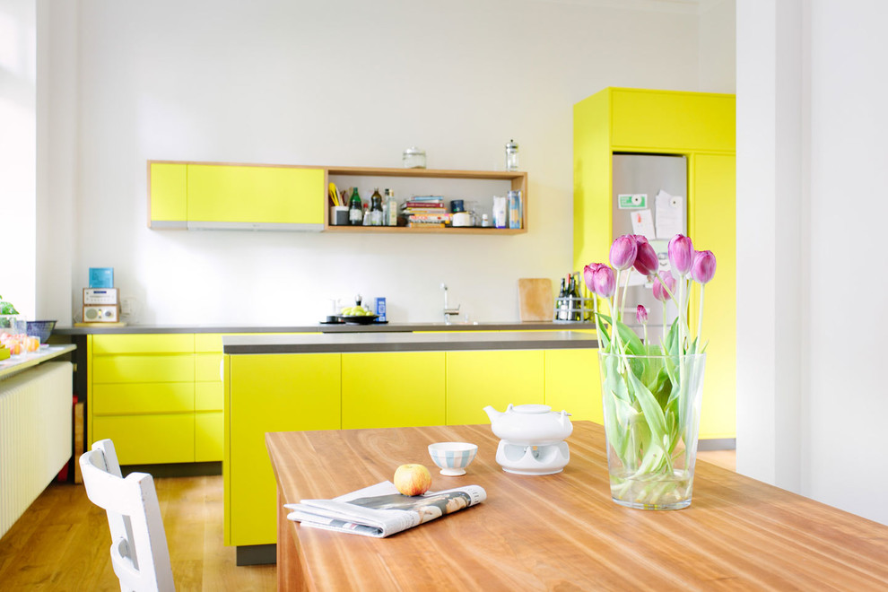 Immagine di una cucina scandinava di medie dimensioni con ante lisce, ante gialle, elettrodomestici in acciaio inossidabile, pavimento in legno massello medio, 2 o più isole e pavimento marrone