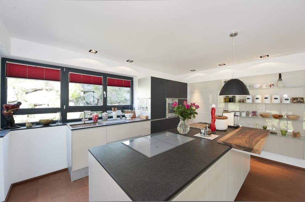 Inspiration for a large contemporary galley open plan kitchen in Other with a submerged sink, flat-panel cabinets, grey cabinets, integrated appliances, an island, limestone worktops, medium hardwood flooring and black splashback.