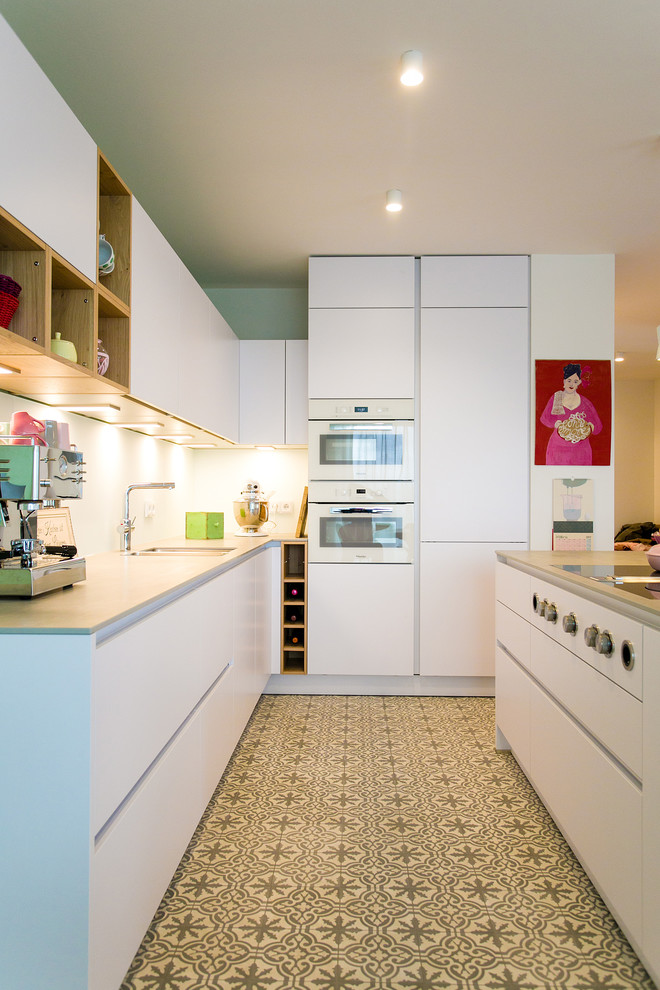 Idéer för ett modernt kök, med en undermonterad diskho, släta luckor, vita skåp, vitt stänkskydd, stänkskydd i glaskakel, vita vitvaror, cementgolv och en köksö
