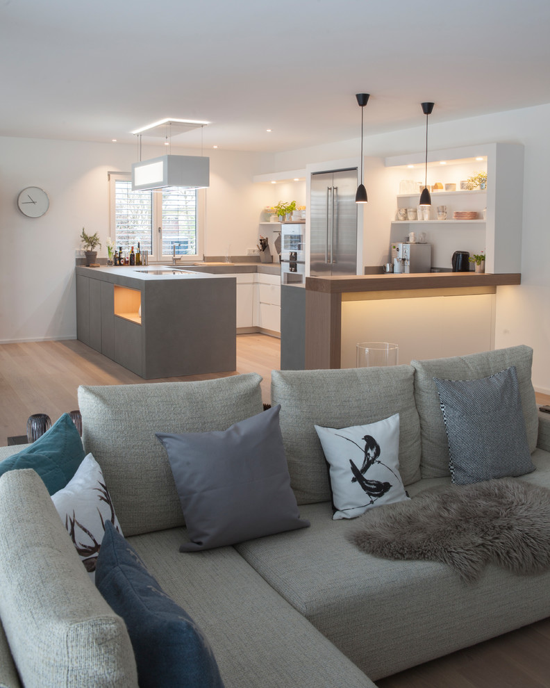 This is an example of a medium sized scandinavian u-shaped open plan kitchen in Munich with flat-panel cabinets, white cabinets, concrete worktops, stainless steel appliances, light hardwood flooring, a breakfast bar, beige floors and grey worktops.