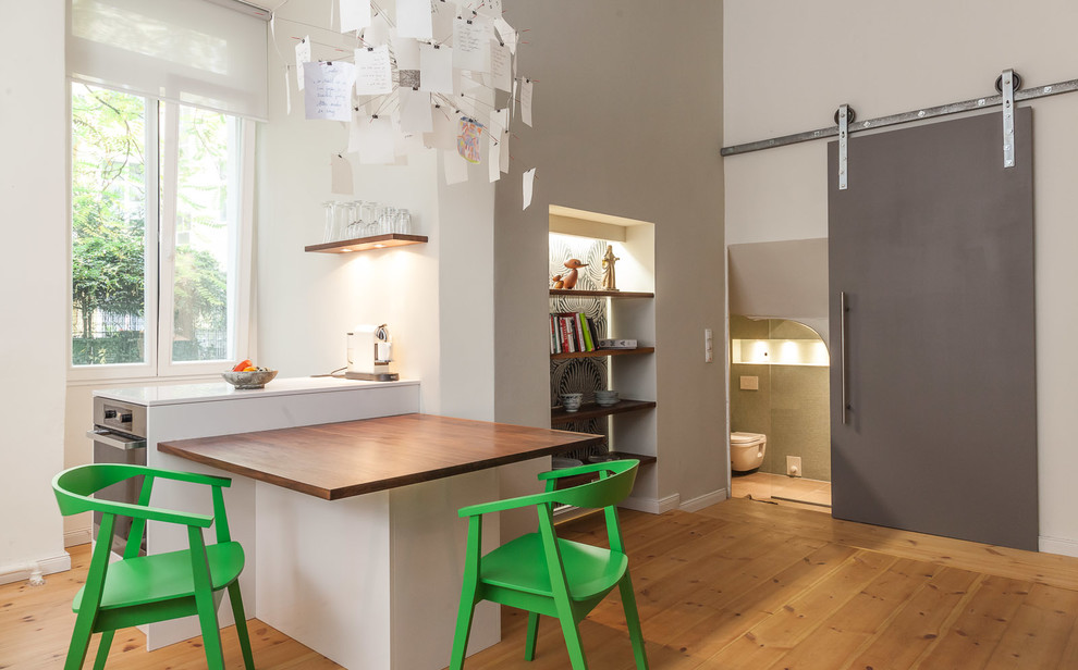 Foto di una piccola cucina ad ambiente unico minimal con elettrodomestici in acciaio inossidabile, pavimento in legno massello medio e penisola