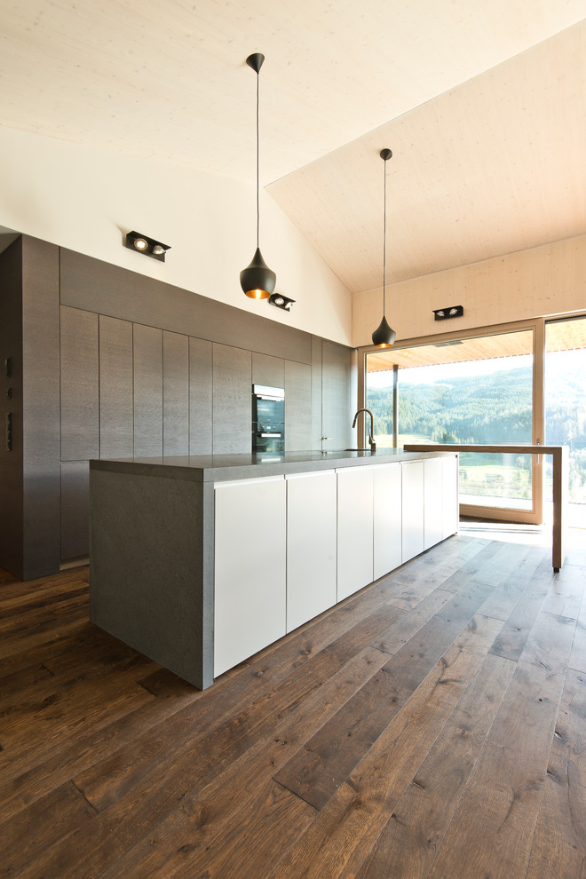 Inredning av ett modernt mellanstort linjärt kök med öppen planlösning, med släta luckor, svarta vitvaror, mellanmörkt trägolv, en köksö och brunt golv