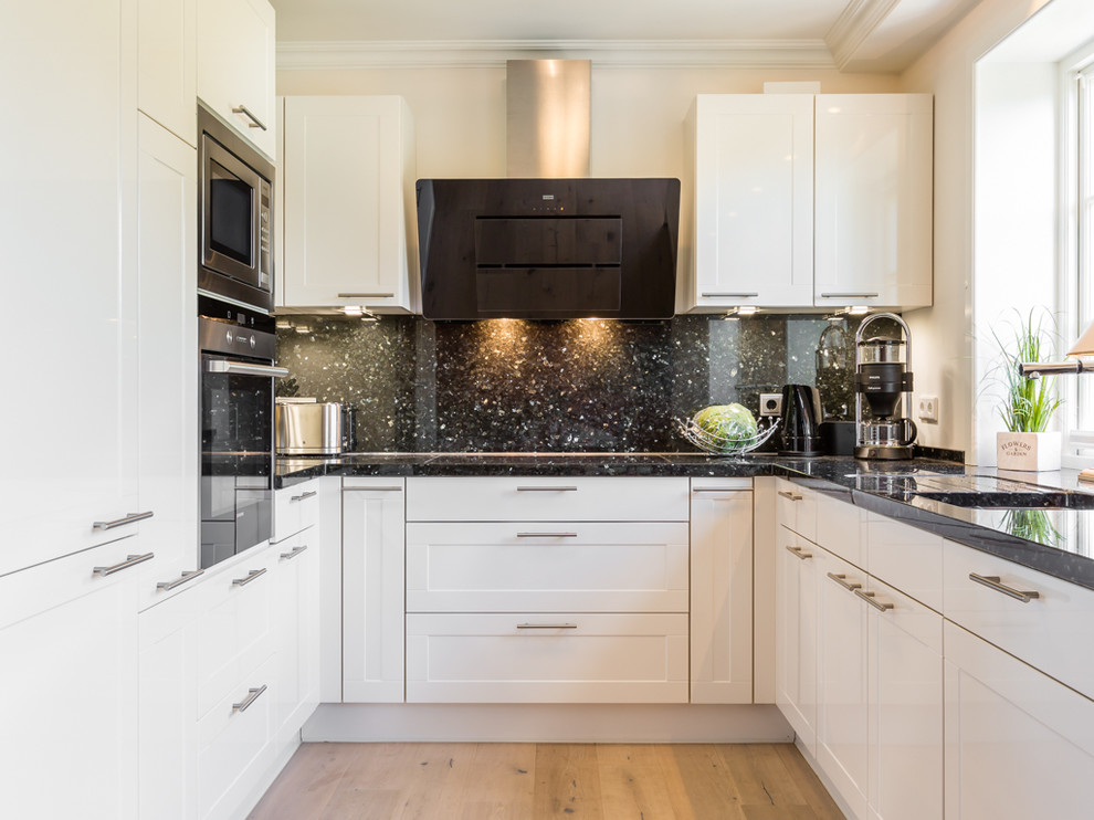 Photo of a medium sized country u-shaped enclosed kitchen in Other with a built-in sink, white cabinets, granite worktops, white splashback, stone tiled splashback, stainless steel appliances, medium hardwood flooring, shaker cabinets and no island.