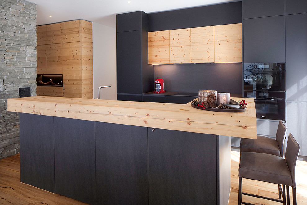 Réalisation d'une cuisine nordique en bois clair avec un placard à porte plane, un plan de travail en bois, un électroménager noir, parquet clair et îlot.