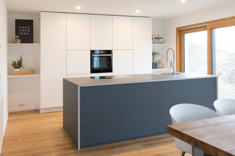 Idéer för att renovera ett stort funkis blå linjärt blått kök med öppen planlösning, med släta luckor, vita skåp, laminatbänkskiva, en köksö, en integrerad diskho, mellanmörkt trägolv och brunt golv