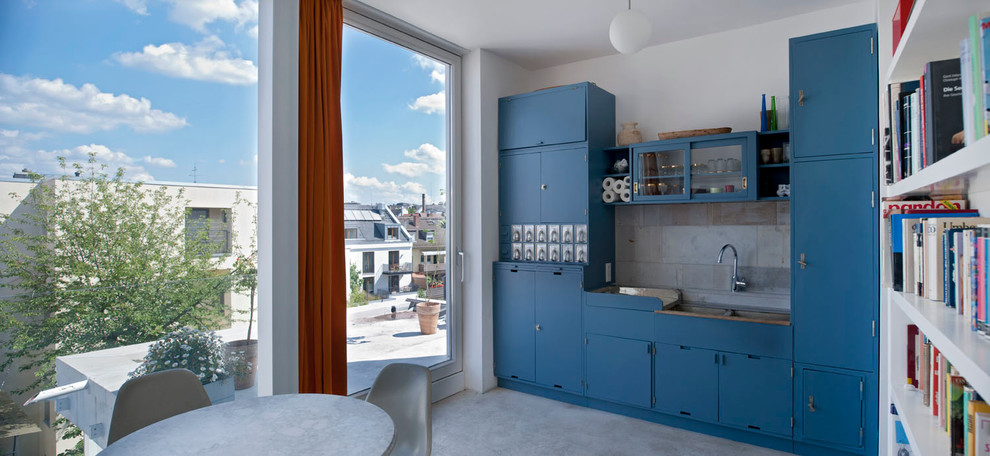 Exempel på ett litet modernt linjärt kök och matrum, med en dubbel diskho, blå skåp, grått stänkskydd, betonggolv, släta luckor, stänkskydd i stenkakel och integrerade vitvaror