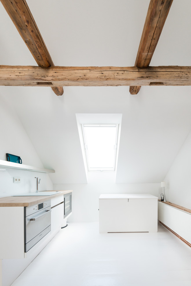 Cette photo montre une petite cuisine linéaire scandinave avec un placard à porte plane, des portes de placard blanches, un plan de travail en bois, une crédence blanche et un sol en linoléum.