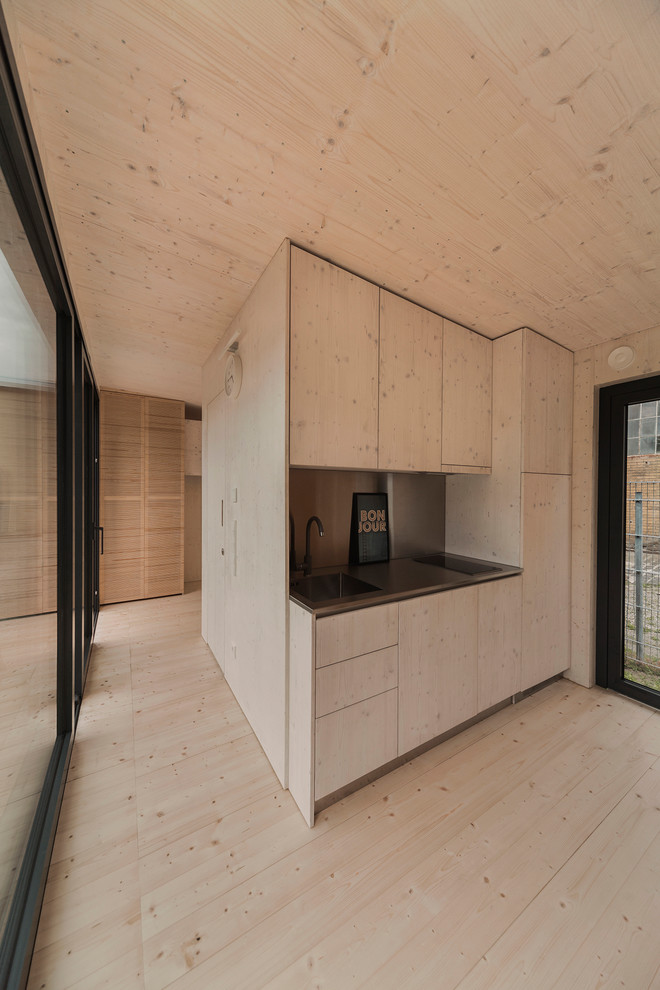 Réalisation d'une petite cuisine ouverte linéaire minimaliste en bois clair avec un placard à porte plane, un plan de travail en inox et parquet clair.