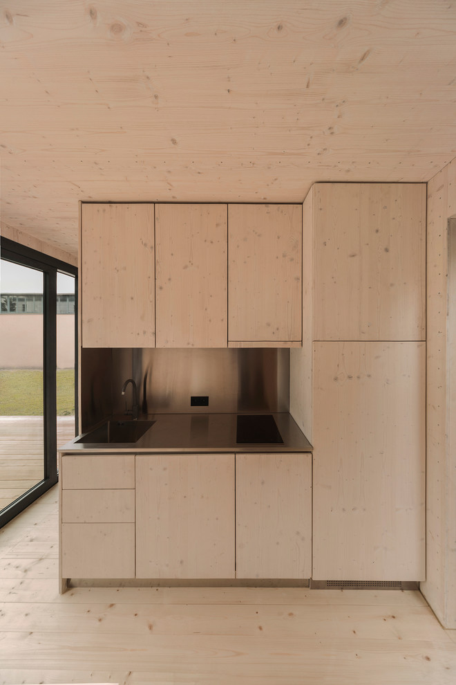 Diseño de cocina lineal nórdica pequeña abierta con armarios con paneles lisos, puertas de armario de madera clara y encimera de acero inoxidable
