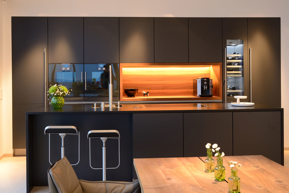 Esempio di una cucina minimalista di medie dimensioni con lavello sottopiano, ante lisce, ante nere, paraspruzzi in legno, elettrodomestici neri, pavimento beige e top nero