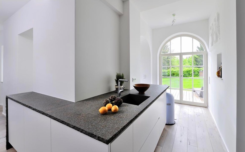 Foto på ett stort funkis kök, med vita skåp, vitt stänkskydd, en integrerad diskho, släta luckor, granitbänkskiva, rostfria vitvaror, ljust trägolv, en halv köksö och brunt golv