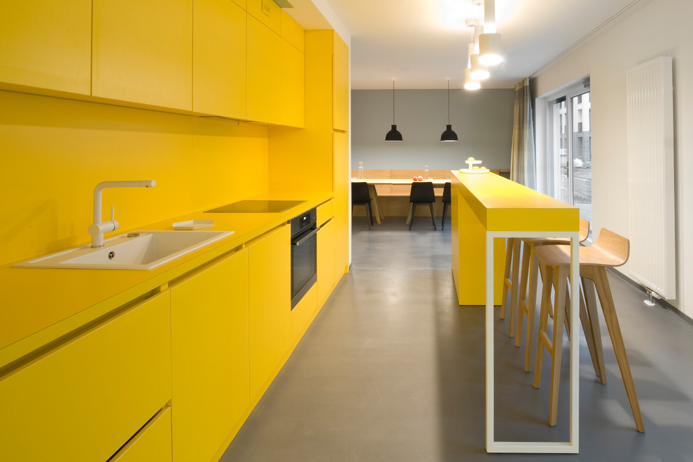 Пример оригинального дизайна: маленькая параллельная кухня-гостиная в современном стиле с накладной мойкой, плоскими фасадами, желтыми фасадами, желтым фартуком, черной техникой, полом из винила, полуостровом и серым полом для на участке и в саду