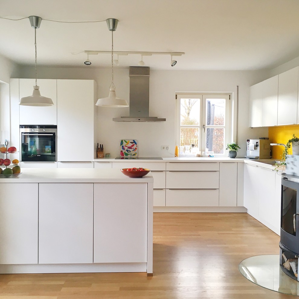 Photo of a large contemporary l-shaped kitchen/diner in Munich with an integrated sink, flat-panel cabinets, white cabinets, yellow splashback, stainless steel appliances, medium hardwood flooring, a breakfast bar and white worktops.