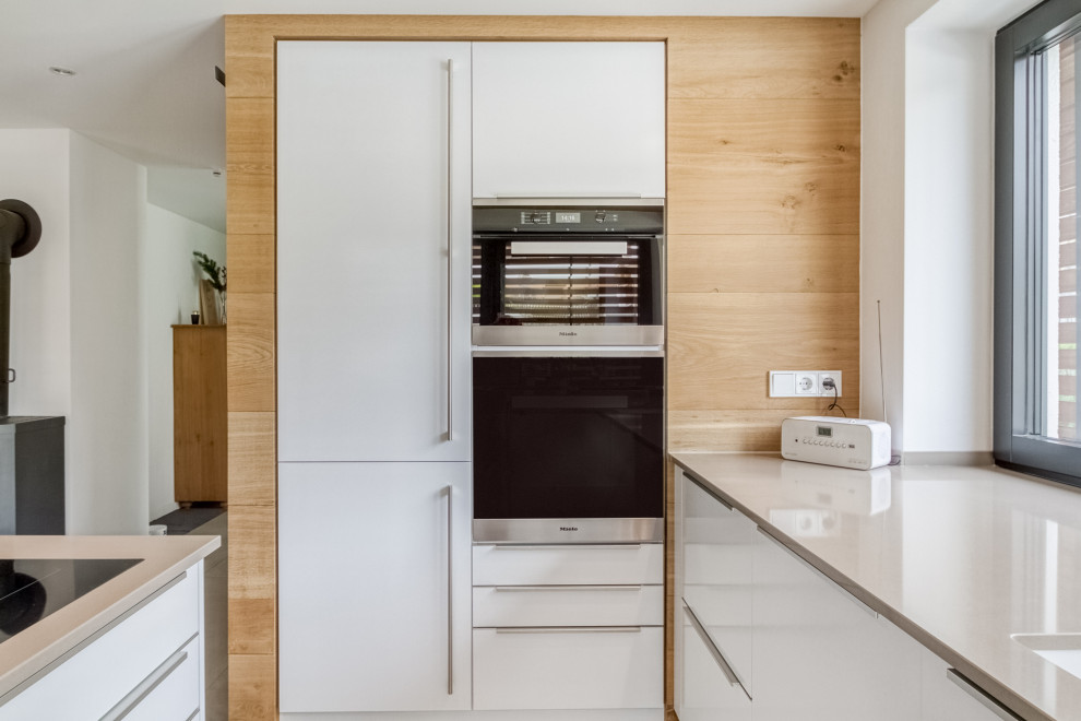 Foto på ett funkis grå kök och matrum, med en undermonterad diskho, släta luckor, vita skåp, svarta vitvaror, en halv köksö och grått golv