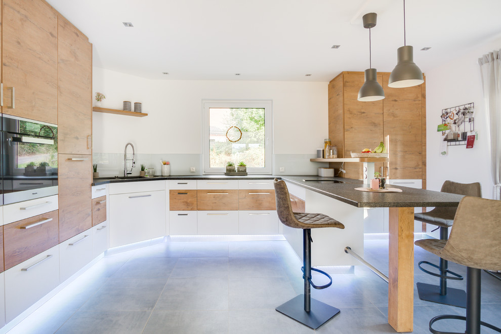 Design ideas for a large contemporary u-shaped open plan kitchen in Frankfurt with an integrated sink, flat-panel cabinets, medium wood cabinets, granite worktops, white splashback, wood splashback, stainless steel appliances, cement flooring, an island, grey floors and grey worktops.
