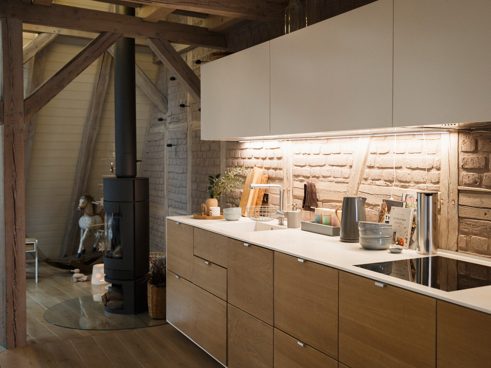 Cette photo montre une petite cuisine ouverte linéaire scandinave en bois brun avec un évier intégré, un placard à porte plane, une crédence marron, une crédence en brique, un électroménager noir, un sol en bois brun, aucun îlot et un sol marron.